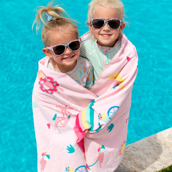 Two girls wrapped in the beach day beach and bath towel at the pool.
