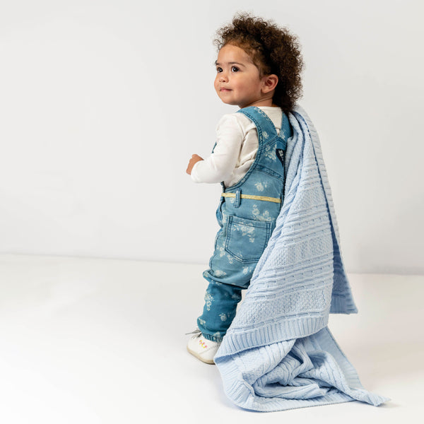 Baby girl holding blue chenille blanket.